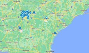 Georgia school violence map: Map of Georgia, US, and some surrounding east coast area in greens and yellows, next to light blue Atlantic Ocean, with darker blue map pins on locations of school violence incidents