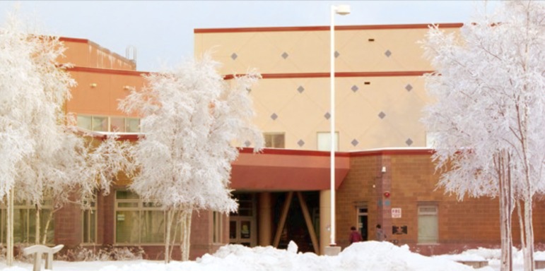 Q&A Civics teacher interview: School campus 2 story building with tan and rust-trimmed second story with red brick first story with snow-covered trees and ground out front