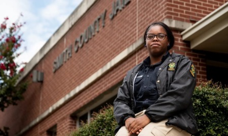 Teens as Texas Jail Guards: Teen girl in tan pants and dark uniform jacket sitting outside a red brick building on a low red brick entryway wall