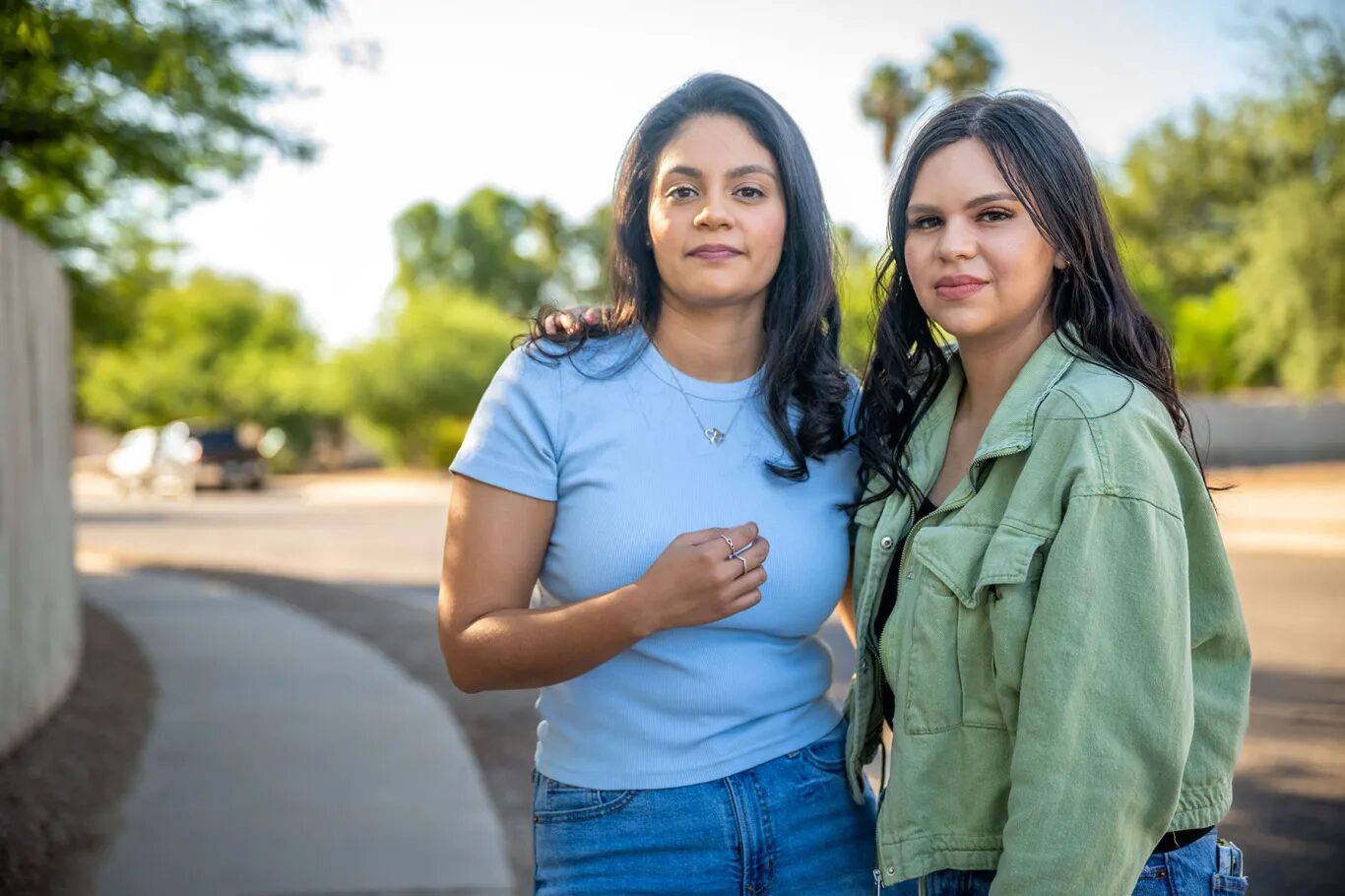 Latino voters gun reform Arizona: Two women with long dar hair stand next to each other with empty street and trees in background