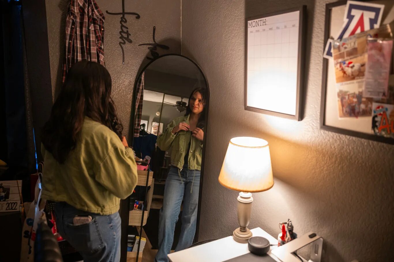 Latino voters gun reform Arizona: Person with bck to camera and long dark hair stands looking at self in tall floor mirror with small lamp on table to her right