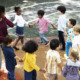 Childcare subsidies: Group of 8 primary students and one female teacher playing outside hold hands while going around in a circle