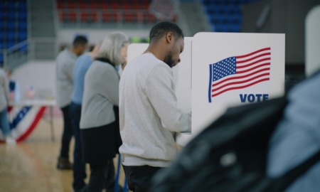 School choice votes: Several people stand in partially enclosed voting booths writing on table top