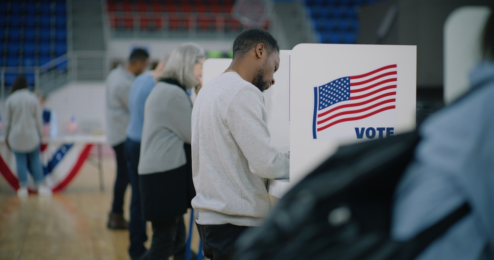 School choice votes: Several people stand in partially enclosed voting booths writing on table top