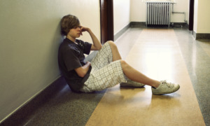 Kentucky foster kids in offices: Older teen boy sits on floor in office hallway