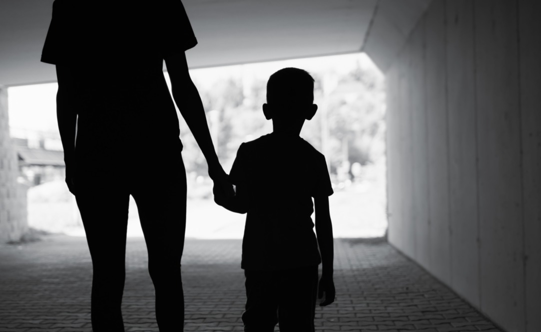 West Virginia foster care: Blac k and white photo of silhouette back of adult holding hand of young child, walking away from camera in dark tunnel toward light outdoor area