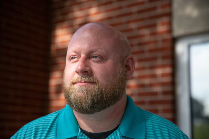 Arming teachers in Tennessee:Headshot of bald white man with light beown fill beard in real polo shirt in front of red brick wall