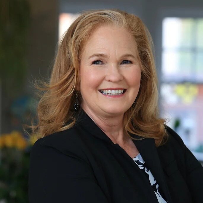 CA foster care shutdown: Whire woman with long red hair in black suit smiles widely into camera