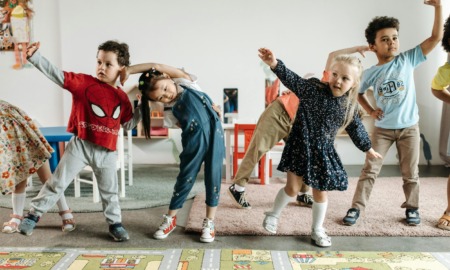 Childcare private equity regulations: Several early primary kids dance and stretch while in a line inside pre-school classroom