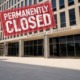 Close DOE Unlikel: DOE building -- beige, multistory, moder --- with red, grungy rectangle sign with white text "Permanently Closed"