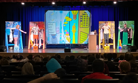 Arts in STEM: Several teens in costumes stand on theater stage with five pieces of art all larger than a person