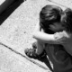 Sexual abuse recovery: Black and white photo of young child sitting on sidewalk with knees up, head down and arms on knees.