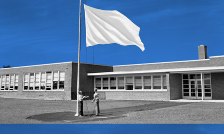 Civic curriculum debate: Two children face each other at very tall flagpole raising an all-white flag up the pole that is on a lawn in front of a one-story brick building with multiple large windows. Blue sky above building.