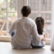 child sexual abuse prevention: back view of dark-haired woman in white shirt with arm round the back of young, dark-haired child, both seated in front of large window looking outside