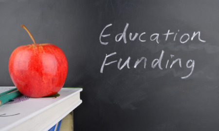 Pandemic school funding: Classroom with red apple,books and handwriting in white chalk on blackboard "Education Funding"