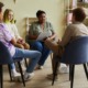 DEI officers needed: Small group of ethnically diverse teens sit in chair circle with Black adult woman leading a discussion and taking notes