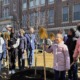 Philadelphia schools get state grant to plant more trees: young students with shovels stand and smile in front of newly planted tree outside school building