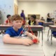 Post-COVID summer programs: young male student at desk shows his pyramid-shaped project