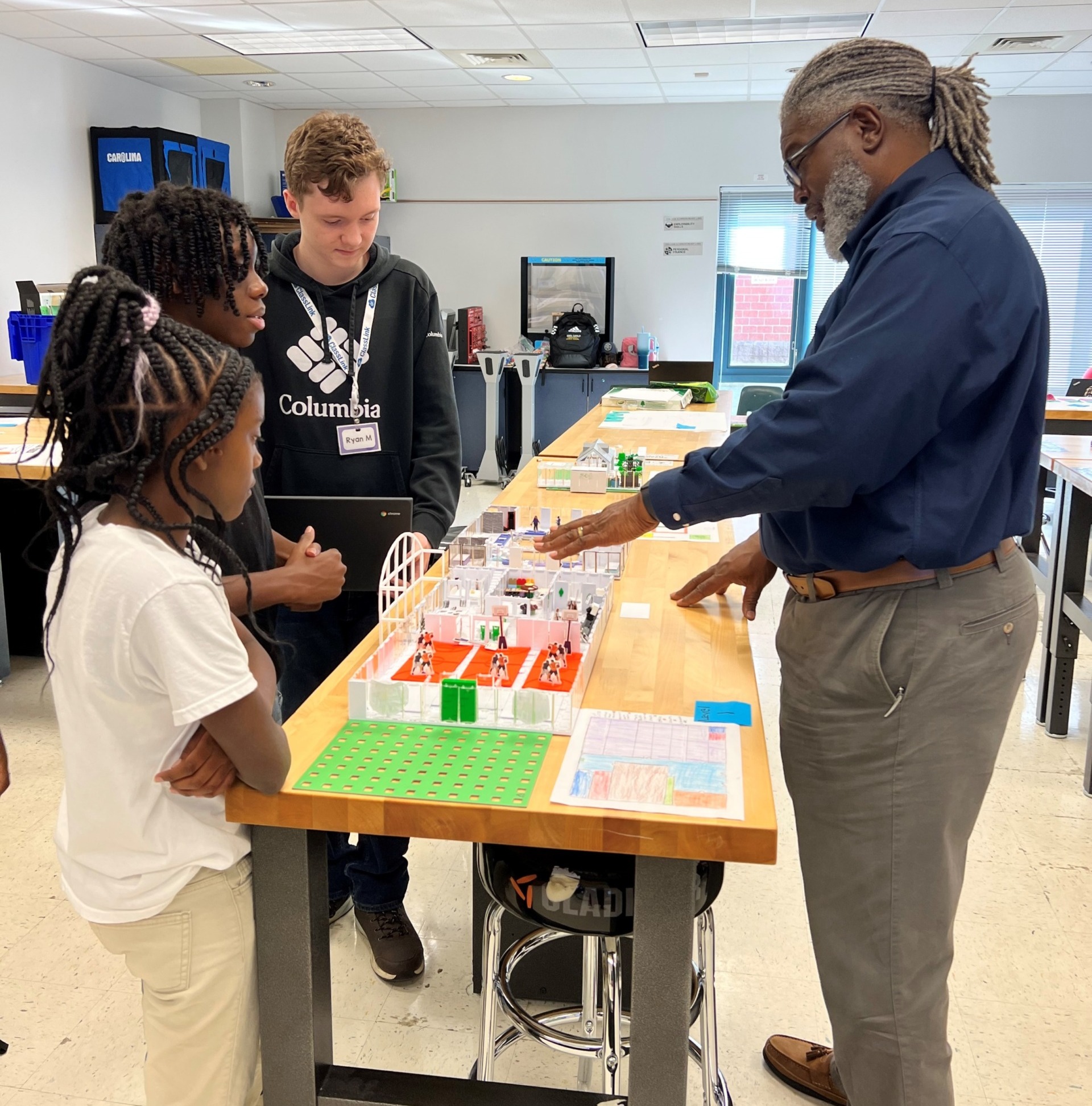 Post-COVID summer programs: teacher works with students at table on design project