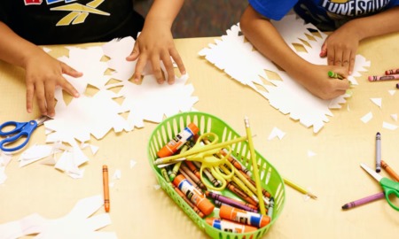 Teacher expenses, what teachers buy for their classrooms with their own money: hands of children working at table with crayons, pencils, glue, scissors and paper