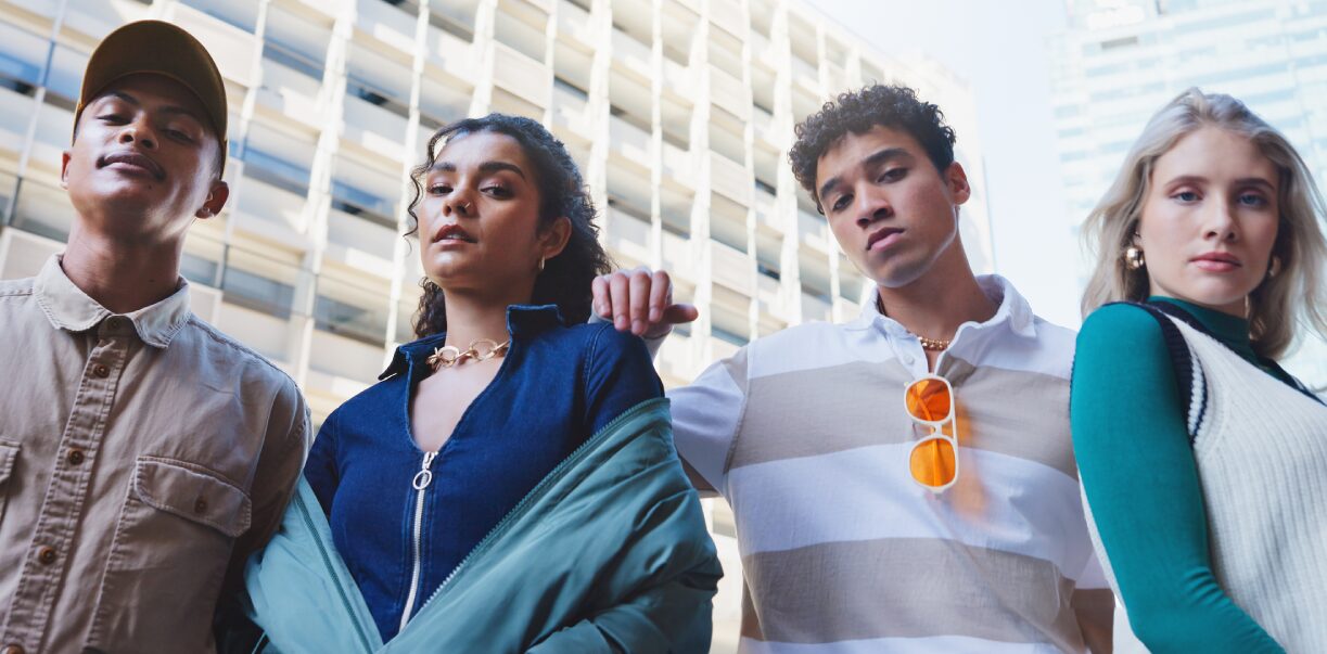 SYSTEM-INVOLVED YOUTH: FOUR TEENS WITH SERIOUS LOOKS ON THEIR FACES STAND NEXT TO EACH OTHER OUTSIDE IN FRONT OF A WHITE SKYSCRAPER