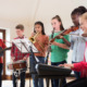 educational opportunity gap: 5 young teen stand and sit playing different musical instruments together