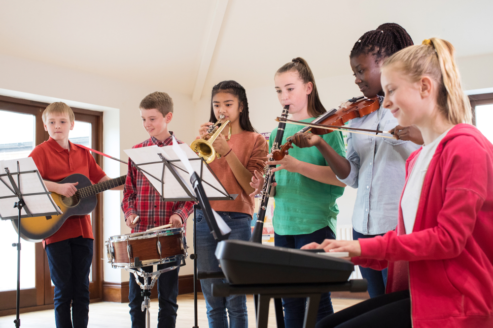 educational opportunity gap: 5 young teen stand and sit playing different musical instruments together