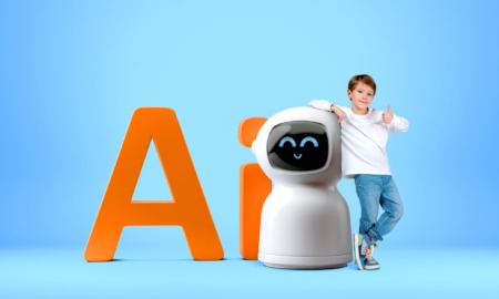 YLeveragig AI in esucation: Young, dark-haired boy in white t-shirt and blue jeans stands next to small, round-heded white robot that is as tall as the boy's shoulder. Orange letters "AI" as large as the robot are behind both of them. All against a plain sky blue backdrop and floor.