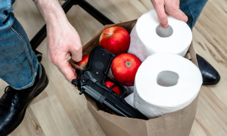 gun violence: A man holding a grocery shopping paper bag with toilet paper, apples, gun