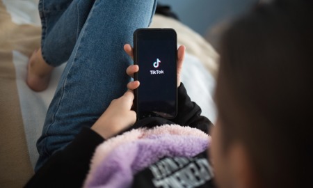 social media use, tiktok, youth mental health: young person laying down opening TikTok on phone