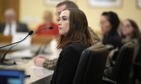 Surge in eating disorders spurs state legislative action: young woman with brown hair looks off to her left while seated at table with microphones