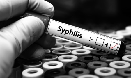 Syphilis is killing babies: black and white image of gloved hand in lab holding positive syphilis test tube