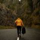 Fute uncertain for person in orange coat walking alone with backback on road surrounded by mountains