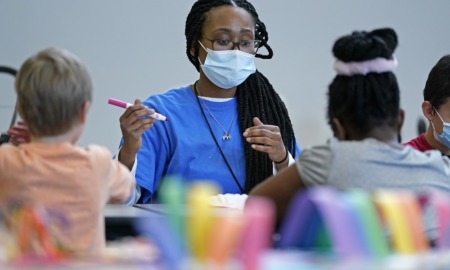 understaffing at after-school programs leaves unmet demand: black woman with long hair with facemask on works at a table with children