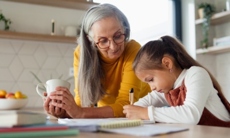 informal child care providers, When grandparents raise grandkids: older woman with long hair holding coffee cup helping young girl with homework