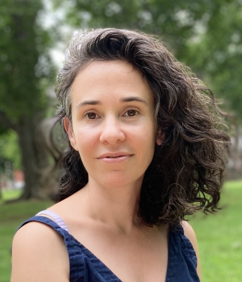 Victoria Restler headshot: Woman with brown, curly hair in sleeveless navy top