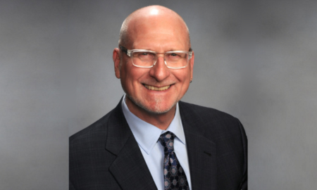 Afterschool California: Michael Funk Headshot bald older man with wirerim glasses in navy suit, light blue shirt and navy tie