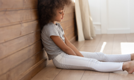 Adults Health Problems Attributable to Adverse Childhood Experiences report; young, sad black girl sitting on floor