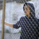 Juvenile justice_youth behind fence: young male offender standing behind chain link fence